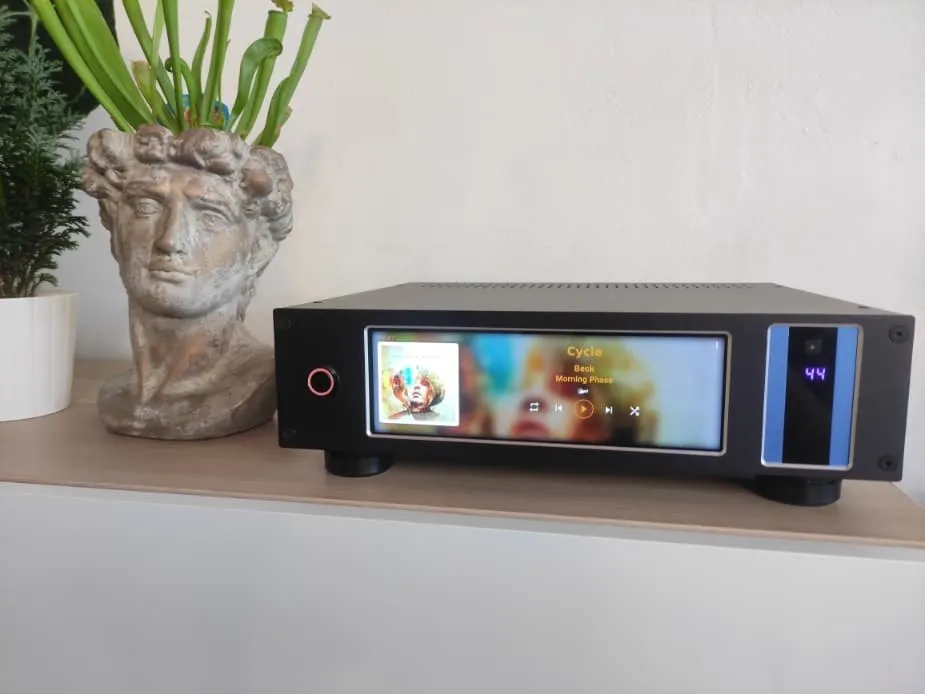 Amplificatore nero compatto con un touchscreen colorato, su uno scaffale