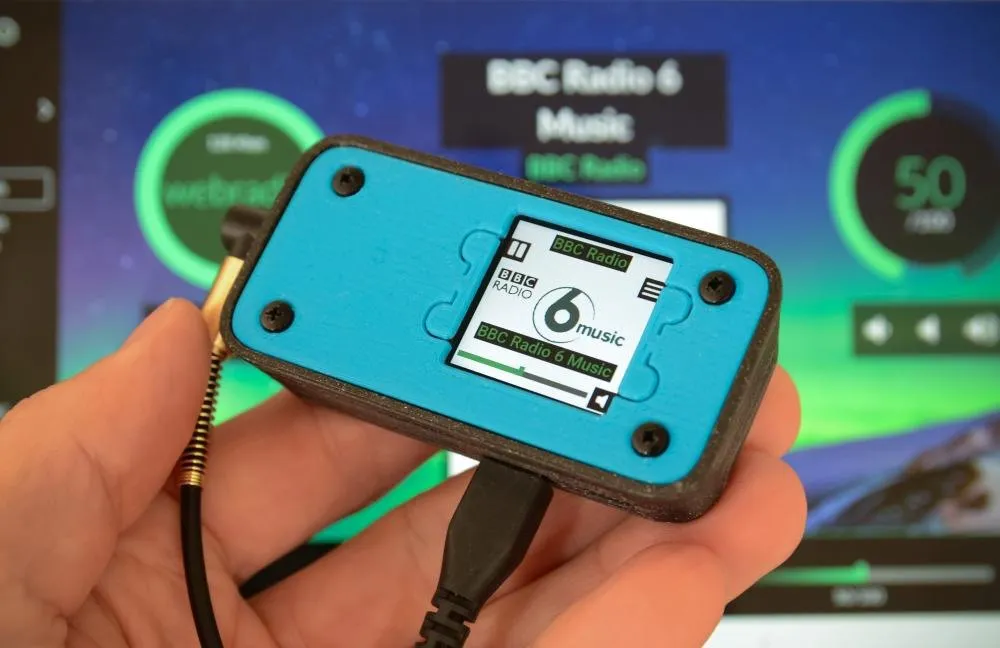 Mano che tiene un piccolo lettore verde acqua stampato in 3D, con un minuscolo schermo