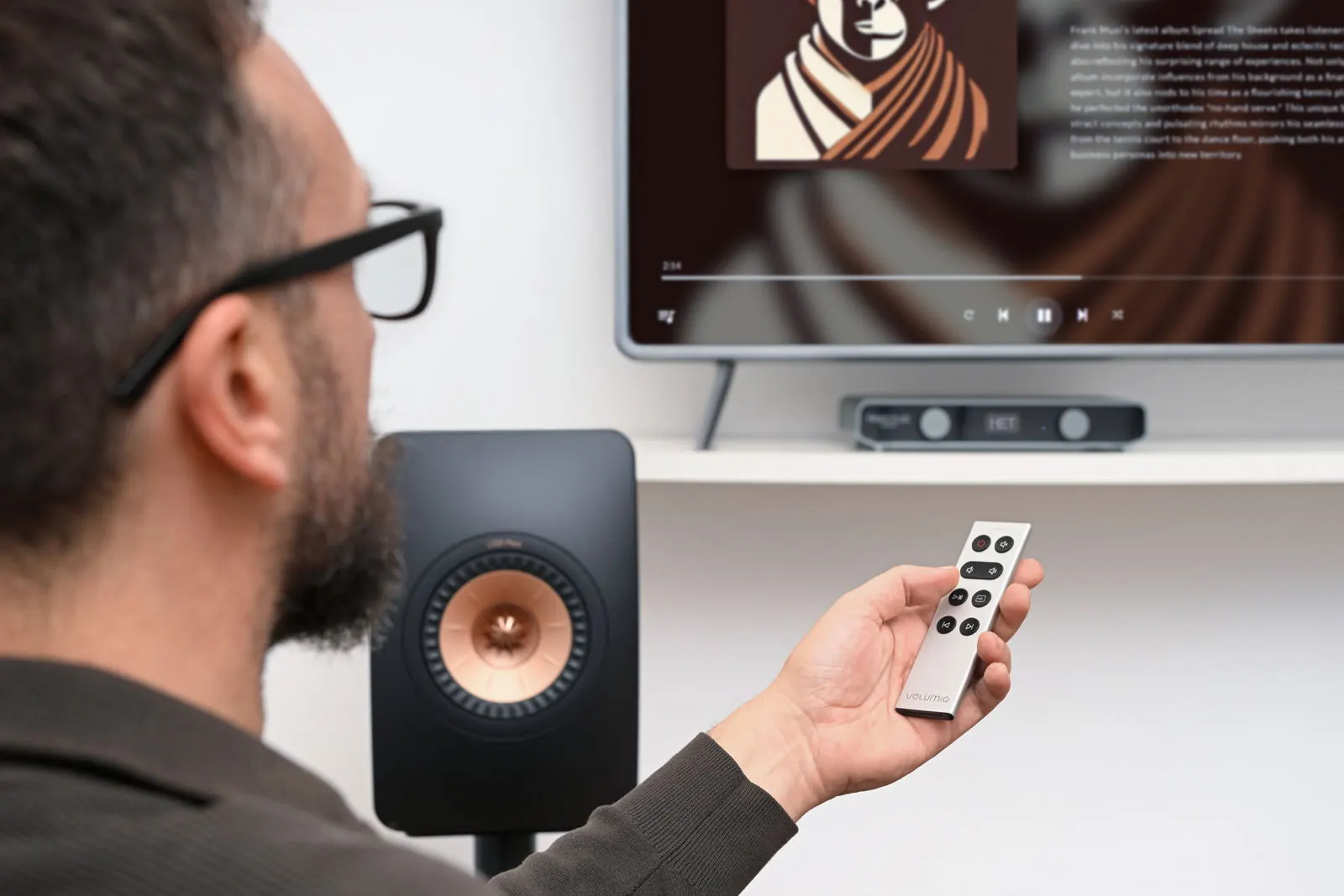 A listener pointing the Remoto remote at Primo Plus, with the TV showing the album playing.