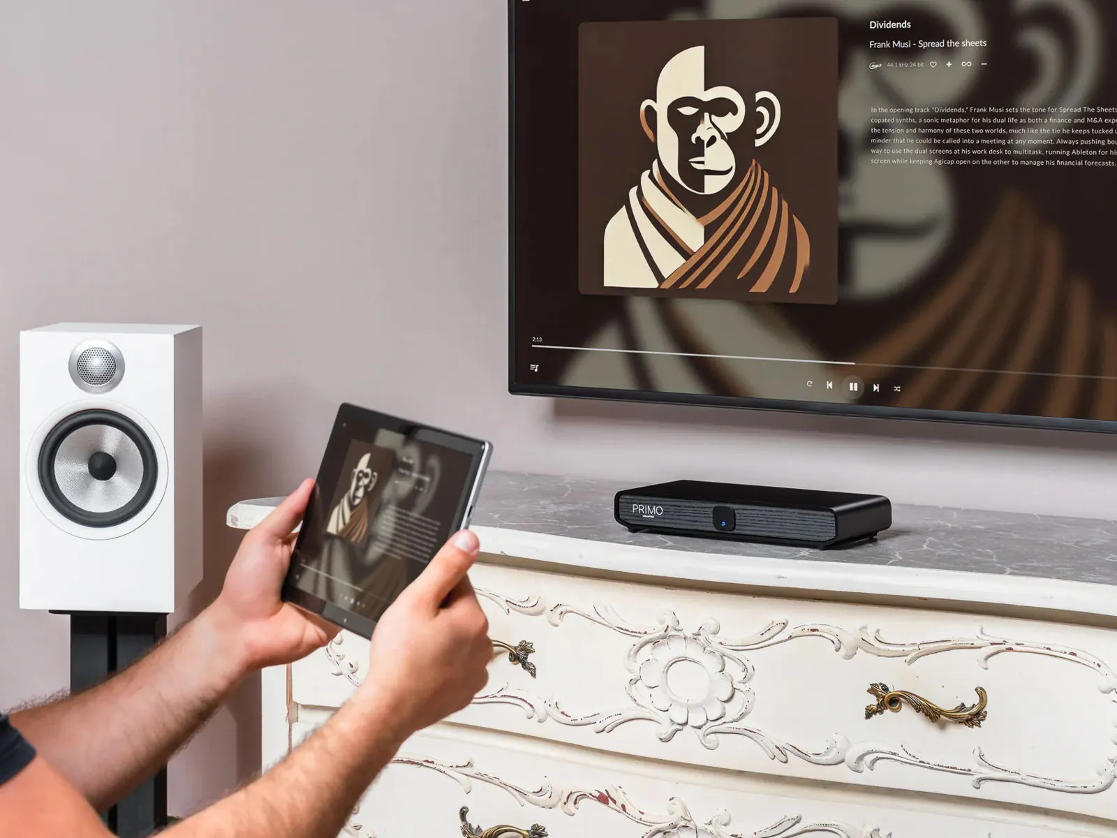 A listener holding a tablet that shows album art, with Primo V3 on a dresser and the same album on the TV above it.