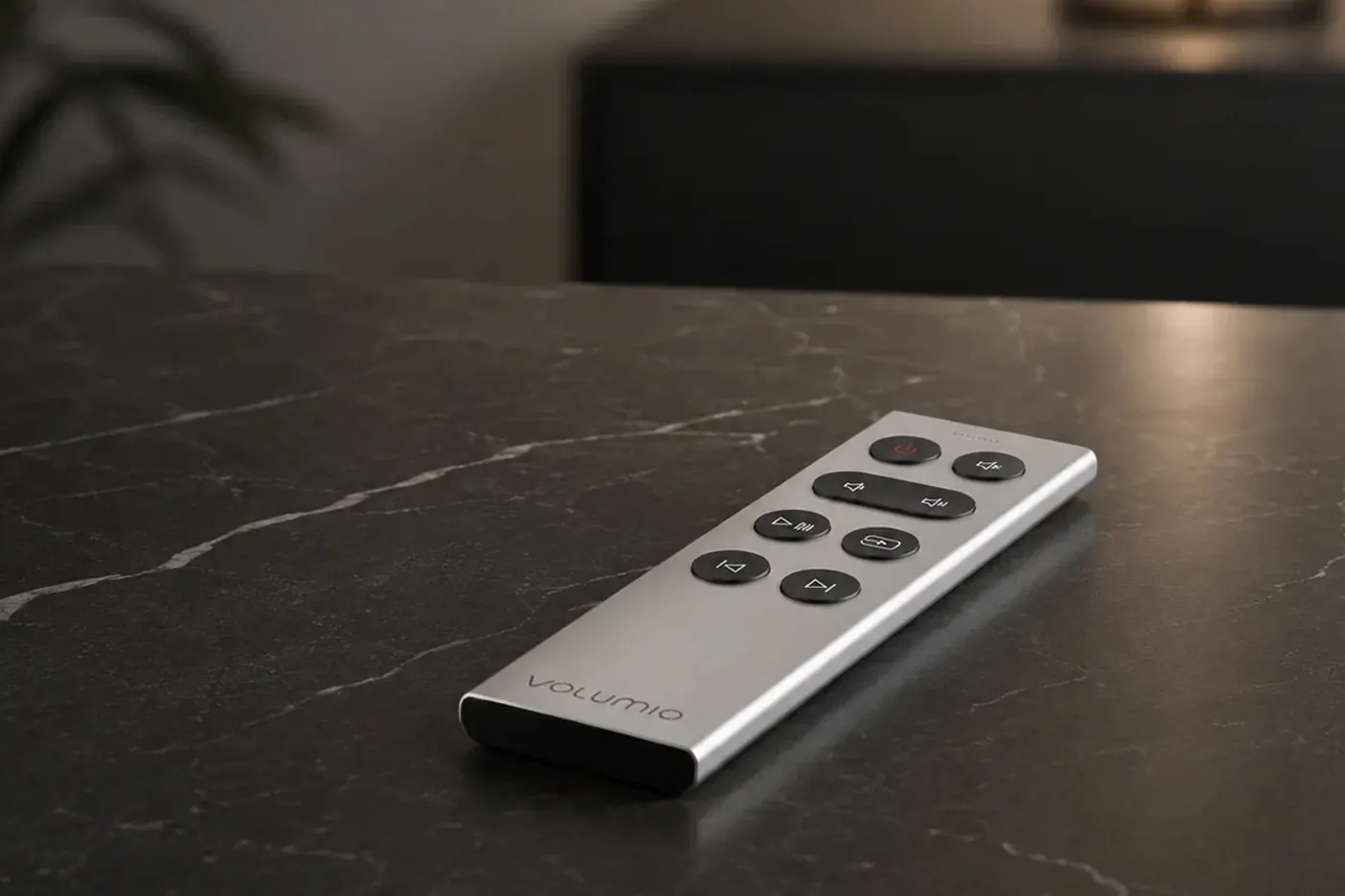 Remoto, a slim silver aluminum remote with black buttons and the Volumio name, on a dark stone table.