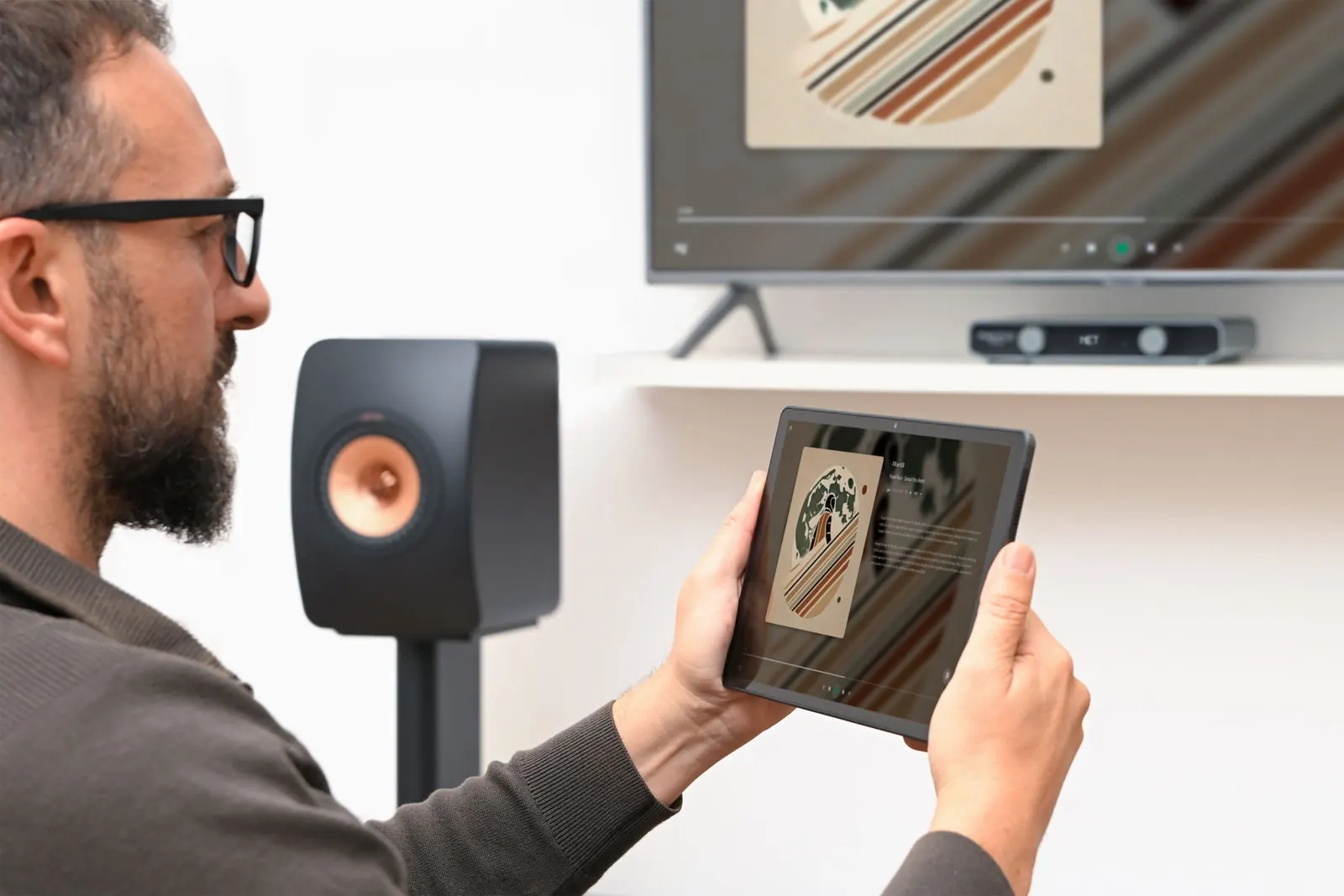 A listener holding a tablet with the Volumio app, next to a speaker and a TV.