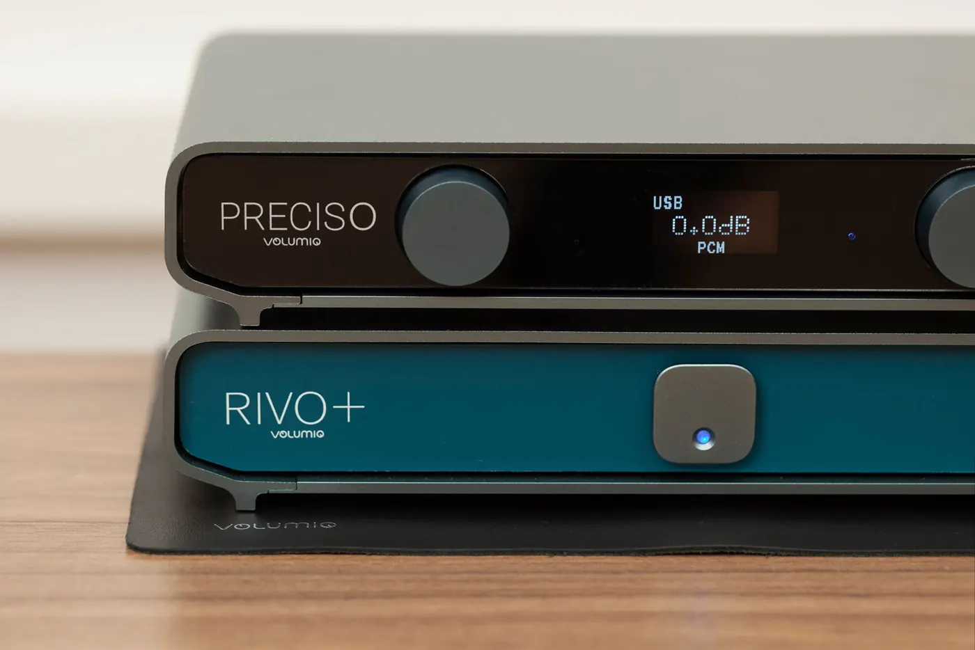 Preciso stacked on top of a Rivo Plus with a blue front, on a black mat on a wooden table. The Preciso display reads USB, 0.0dB and PCM.